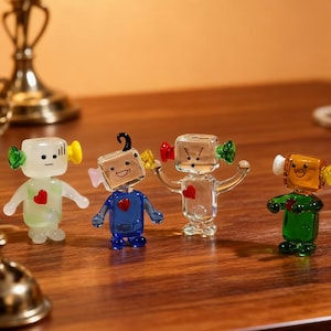 Può includere: Quattro figurine di robot in vetro colorato con dettagli a forma di cuore. Ogni robot ha una diversa combinazione di colori: verde, blu, trasparente e giallo. Hanno braccia e gambe piccole e sono esposti su una superficie di legno.