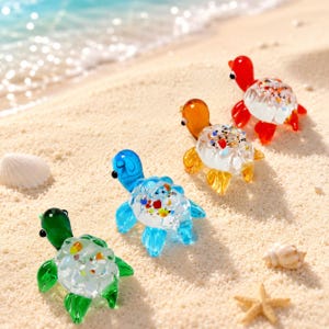 May include: Four colorful glass turtle figurines on a sandy beach. The turtles are in shades of green, blue, orange, and red, with clear shells filled with colorful accents. A seashell and starfish are also visible.