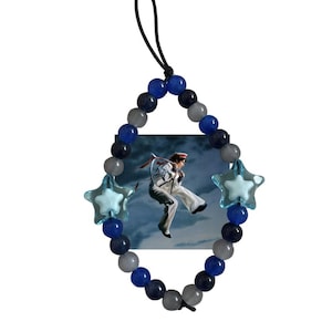May include: A decorative car charm featuring a photo of a person skydiving, surrounded by a beaded strand. The strand is composed of blue, gray, and black beads, with two light blue star-shaped accents. A black cord is attached for hanging.