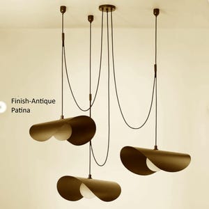 May include: Three pendant lights with an antique patina finish, featuring dark brown, curved shades and white, rounded interiors. They hang from black cords. The image includes the text "Finish-Antique Patina".