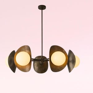 May include: A modern chandelier with a dark bronze finish. It features five spherical, warm-toned light bulbs encased in asymmetrical, metallic shades. The fixture hangs from a central rod, creating a stylish lighting element.