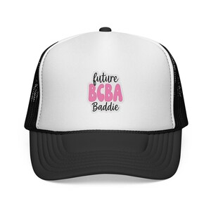 May include: A black and white trucker hat with a curved brim. The front panel is white with the text "future BCBA Baddie" in black script and pink bubble letters. The hat has a mesh back.