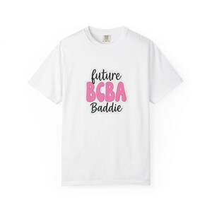 Peut inclure: T-shirt blanc avec l'inscription "future BCBA Baddie" en noir et rose. Le t-shirt a un col rond et des manches courtes. Le texte est centré sur le devant du t-shirt.
