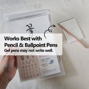 May include: A clear plastic pouch containing educational practice sheets with Korean characters and illustrations, including the text 'Works Best with Pencil & Ballpoint Pens. Gel pens may not write well.' A wooden pencil rests on a small white notepad.