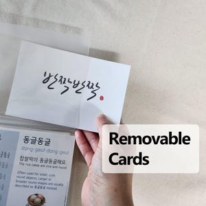 May include: A white rectangular card featuring black Korean calligraphy text that reads 반짝반짝 with a small red circular stamp. The card is partially inserted into a clear plastic sleeve, which also contains a secondary card with Korean text.