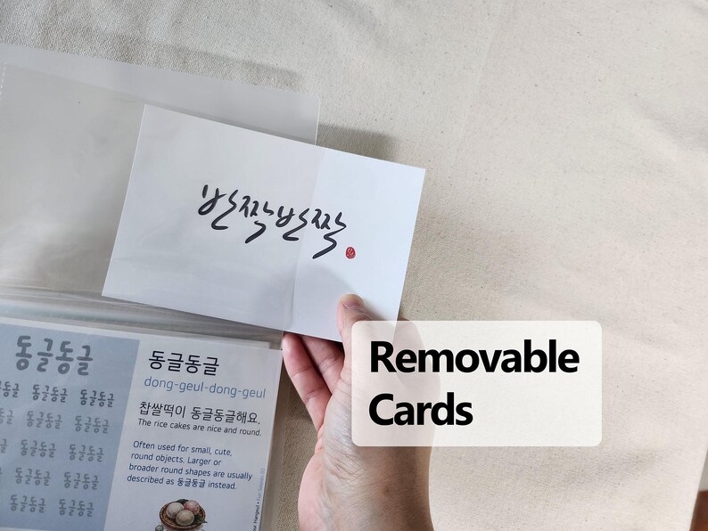 May include: A white rectangular card featuring black Korean calligraphy text that reads 반짝반짝 with a small red circular stamp. The card is partially inserted into a clear plastic sleeve, which also contains a secondary card with Korean text.