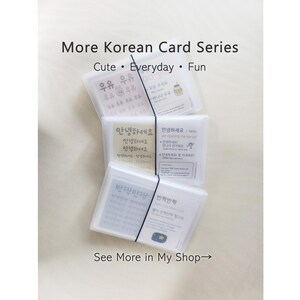 May include: A set of three translucent plastic cases containing Korean language learning cards, stacked vertically and secured with a black elastic band. Each card features Korean text, English translations, and illustrations.