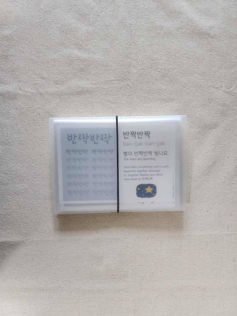 May include: A rectangular, translucent plastic case secured with a thin black elastic band, containing a stack of cards. The visible card features the Korean text '반짝반짝', the romanization 'ban-jjak-ban-jjak', and an illustration of a yellow star.