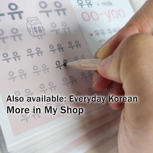May include: A light-colored educational worksheet featuring rows of the Korean Hangul characters for milk, written as '우유', alongside a small cartoon milk carton illustration, with text including 'oo-yoo' and 'milk' printed in black and red ink.