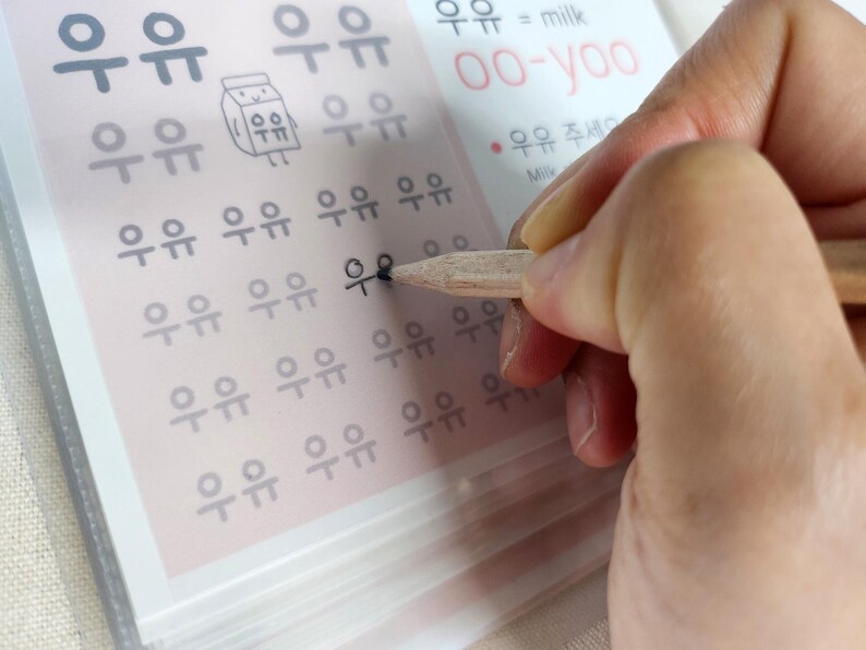 May include: A language learning worksheet featuring rows of the Korean characters for milk, written as 우유, with a small cartoon milk carton illustration, the phonetic pronunciation oo-yoo, and the English translation milk printed in black and red ink.