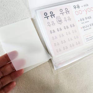 May include: A clear plastic sleeve containing a set of educational cards with Korean text. The top card features the word 우유, the English translation milk, the pronunciation oo-yoo, and illustrations of milk cartons with Korean phrases and text.