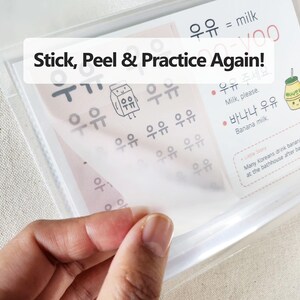 May include: A clear plastic sheet with Korean language practice exercises, featuring the text Stick, Peel & Practice Again!, illustrations of milk cartons, and Korean characters with English translations for milk and banana milk.