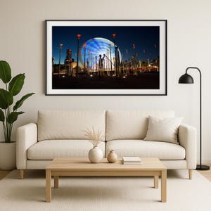 以下が含まれることがあります： 夜の観覧車の額入り写真。青と白の光で照らされています。画像は、光の筋がダイナミックな効果を生み出し、動いている車輪を捉えています。赤いトップが付いた高くて細い街灯が車輪を囲んでいます。