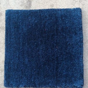 Puede incluir: Una alfombra rectangular azul marino con una superficie texturizada y afelpada. La alfombra se muestra sobre una superficie de hormigón. Esta alfombra es adecuada para la decoración del hogar.