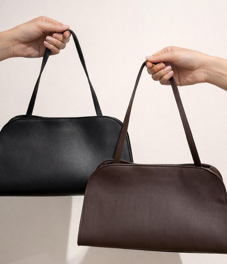 May include: Two shoulder bags are held up against a white background. One bag is black, and the other is brown. Both bags have a rectangular shape with rounded edges and long, thin straps.
