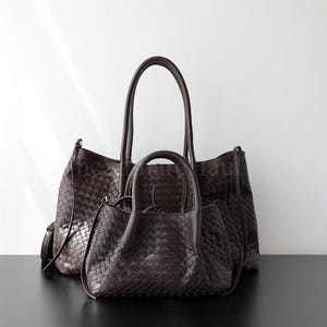 Puede incluir: Tres bolsos de mano de cuero trenzado marr&oacute;n oscuro de diferentes tama&ntilde;os se muestran sobre un fondo blanco. El bolso m&aacute;s grande tiene asas largas, el bolso del medio tiene asas m&aacute;s cortas y el bolso m&aacute;s peque&ntilde;o tiene un asa superior.