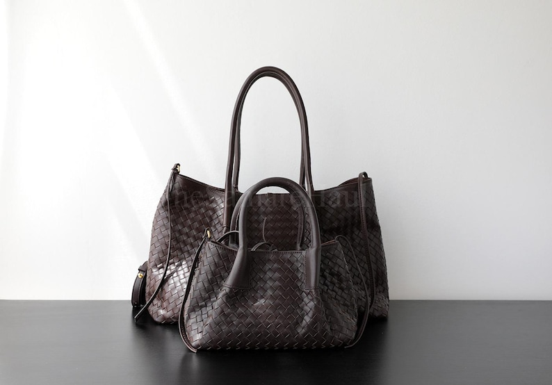 Puede incluir: Tres bolsos de mano de cuero trenzado marr&oacute;n oscuro de diferentes tama&ntilde;os se muestran sobre un fondo blanco. El bolso m&aacute;s grande tiene asas largas, el bolso del medio tiene asas m&aacute;s cortas y el bolso m&aacute;s peque&ntilde;o tiene un asa superior.