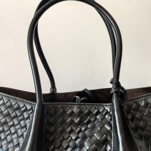 Top handle detail of black woven leather tote bag with smooth leather straps
