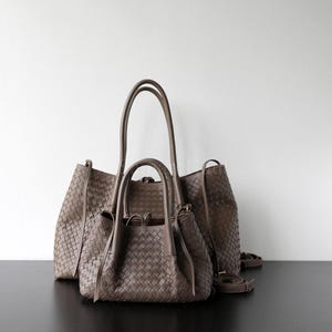 Puede incluir: Dos bolsos de mano de cuero tejido en color topo neutro. El bolso m&aacute;s grande tiene asas altas y una correa para el hombro, mientras que el bolso m&aacute;s peque&ntilde;o tiene asas m&aacute;s cortas. Ambos bolsos tienen un dise&ntilde;o tejido.