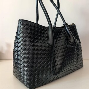 Puede incluir: Bolso tote de cuero negro tejido con dos asas superiores. El bolso presenta un dise&ntilde;o de tejido de cesta y una forma estructurada. Las asas son lisas y el bolso parece nuevo.