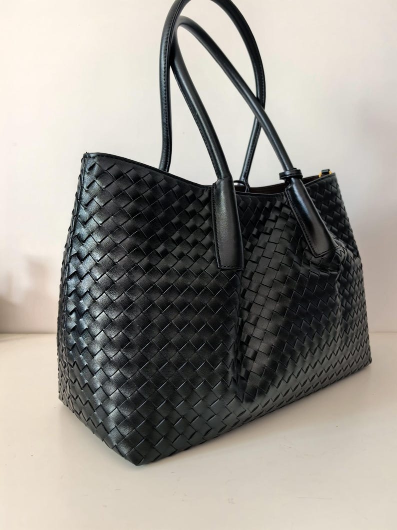 Puede incluir: Bolso tote de cuero negro tejido con dos asas superiores. El bolso presenta un dise&ntilde;o de tejido de cesta y una forma estructurada. Las asas son lisas y el bolso parece nuevo.