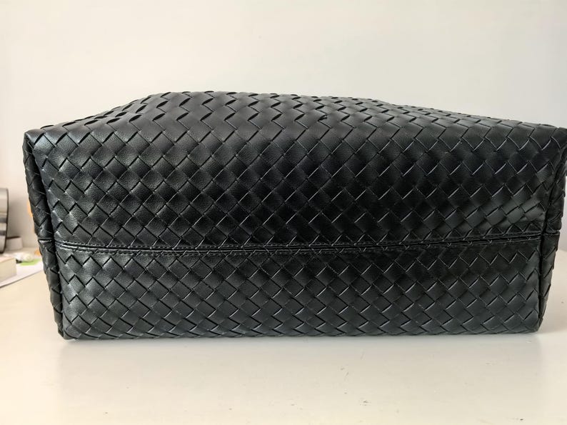 Puede incluir: Bolso tote de cuero negro con un dise&ntilde;o tejido en forma de cesta. El bolso tiene forma rectangular y una base robusta. El cuero parece liso y el tejido est&aacute; bien construido.