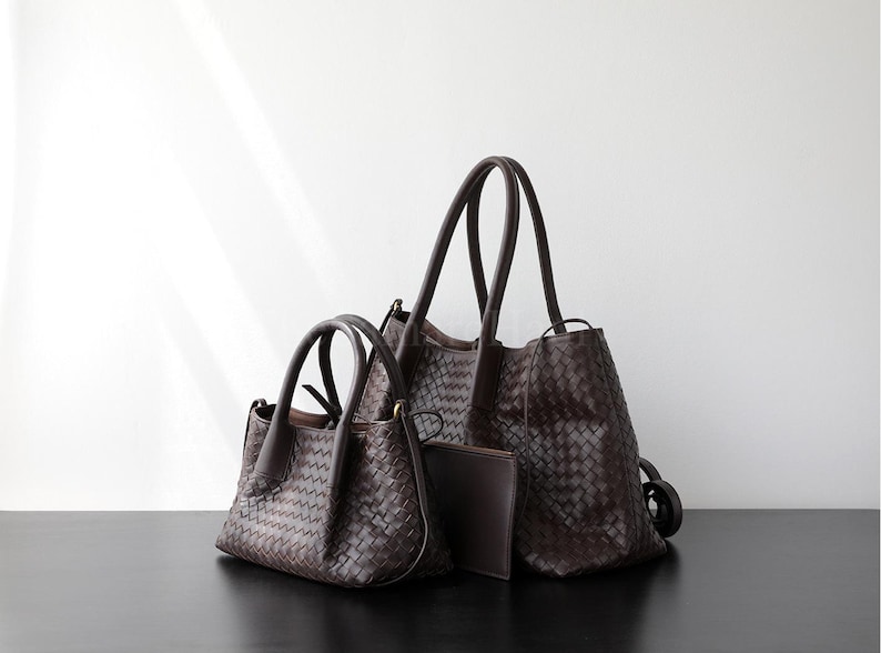Puede incluir: Tres bolsos de mano de cuero marr&oacute;n de diferentes tama&ntilde;os se muestran sobre un fondo blanco. Los bolsos tienen texturas tejidas y asas resistentes. Tambi&eacute;n hay un peque&ntilde;o embrague. Los bolsos est&aacute;n sobre una superficie negra.
