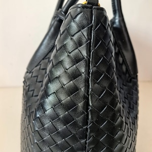 Puede incluir: Un bolso tote de cuero negro con un patr&oacute;n tejido. El bolso tiene dos asas y una forma estructurada. El cuero parece liso y el tejido es apretado, creando una superficie texturizada.