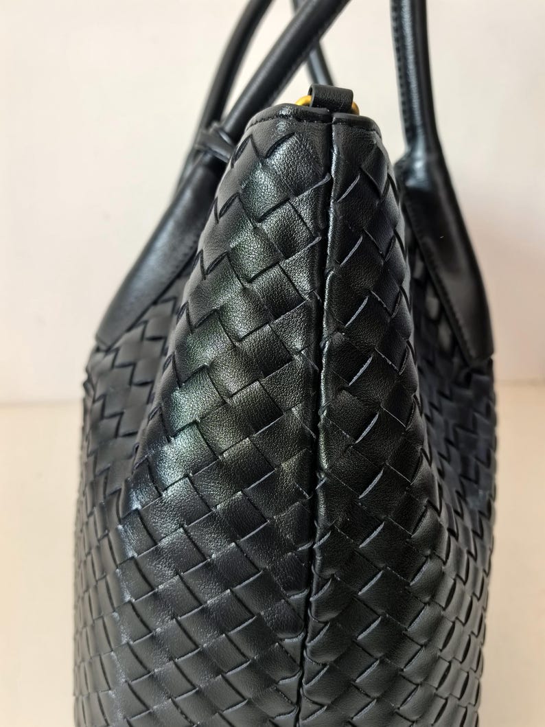 Puede incluir: Un bolso tote de cuero negro con un patr&oacute;n tejido. El bolso tiene dos asas y una forma estructurada. El cuero parece liso y el tejido es apretado, creando una superficie texturizada.