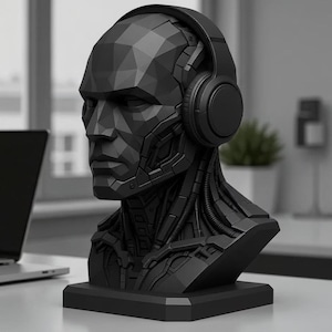 Puede incluir: Busto negro y geométrico de una cabeza humana con auriculares. La escultura tiene una estética futurista y robótica con líneas y ángulos detallados. El busto se asienta sobre una base cuadrada y el fondo está borroso.