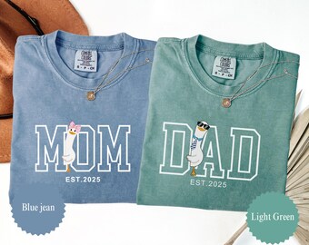 May include: Two Comfort Colors t-shirts, one blue jean and one light green. The blue shirt says "MOM" with a goose graphic and "EST.2025". The green shirt says "DAD" with a goose graphic and "EST.2025". Both shirts have a gold necklace.