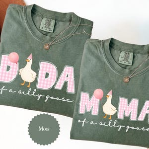 May include: Two moss green t-shirts with the words "DADA" and "MAMA" in pink gingham print, each with a cartoon goose holding a balloon. The text "of a silly goose" is below the words. Each shirt has a small gold necklace.