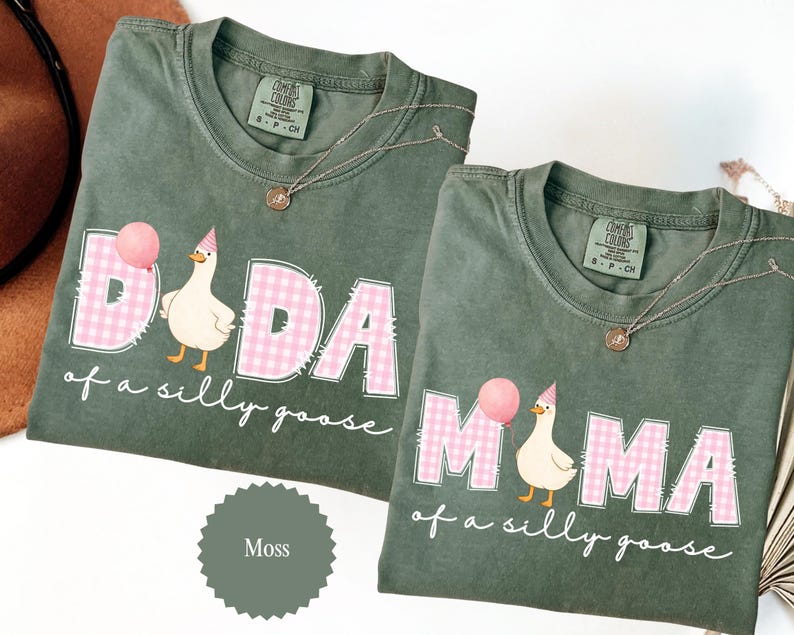 May include: Two moss green t-shirts with the words "DADA" and "MAMA" in pink gingham print, each with a cartoon goose holding a balloon. The text "of a silly goose" is below the words. Each shirt has a small gold necklace.