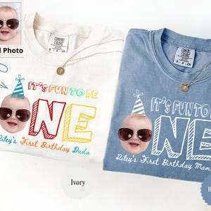 May include: Ivory and blue jean t-shirts with the text "IT'S FUN TO BE ONE" and a baby graphic wearing sunglasses and a party hat. The ivory shirt says "Riley's First Birthday Dada" and the blue jean shirt says "Riley's First Birthday Mama".