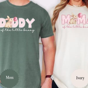 May include: Two t-shirts, one moss green and one ivory, featuring Easter-themed designs. The moss green shirt says "Daddy of the little bunny" with a bunny graphic. The ivory shirt says "Mama of the little bunny".