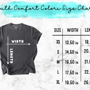May include: A dark gray t-shirt with a size chart for Youth Comfort Colors. The chart lists sizes XS to XL, with corresponding width and length measurements in inches. The shirt has a crew neck and rolled-up sleeves.