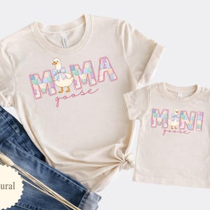 K&ouml;nnte beinhalten: Zwei cremefarbene T-Shirts, eine Erwachsenen- und eine Kindergr&ouml;&szlig;e, mit passenden Designs. Das T-Shirt f&uuml;r Erwachsene sagt "MAMA goose" mit einer G&auml;nseillustration. Das Kinder-T-Shirt sagt "MINI goose". Beide Shirts haben ein pastellfarbenes Patchwork-Design.