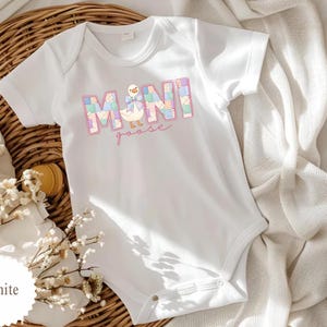 K&ouml;nnte beinhalten: Wei&szlig;er Baby-Body mit dem Text "MINI goose" in einem pastellfarbenen Blockdesign. Der Body zeigt eine Cartoon-Gans-Illustration mit einer Schleife. Das Kleidungsst&uuml;ck ist aus weichem Material und f&uuml;r Babys konzipiert.