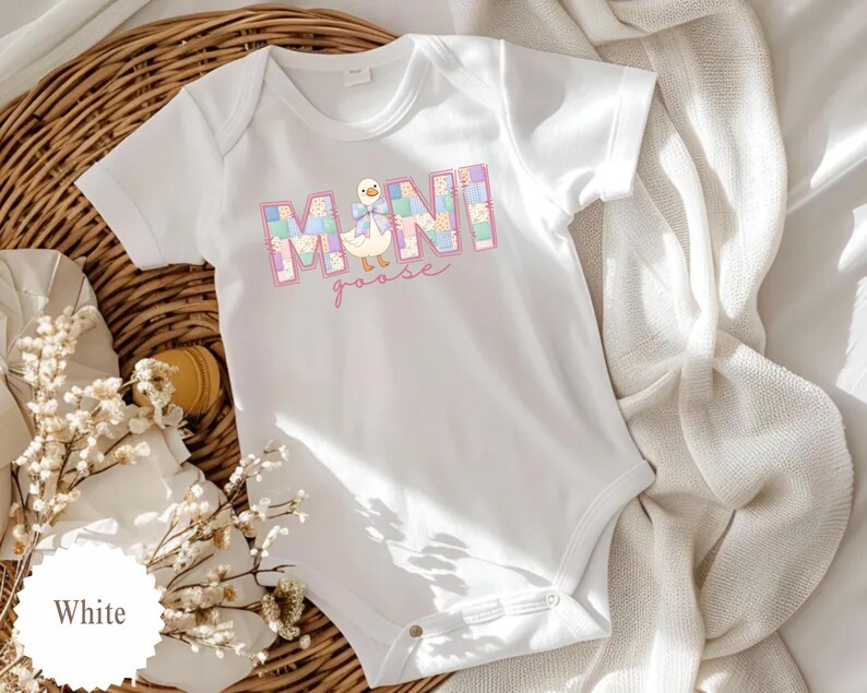 K&ouml;nnte beinhalten: Wei&szlig;er Baby-Body mit dem Text "MINI goose" in einem pastellfarbenen Blockdesign. Der Body zeigt eine Cartoon-Gans-Illustration mit einer Schleife. Das Kleidungsst&uuml;ck ist aus weichem Material und f&uuml;r Babys konzipiert.