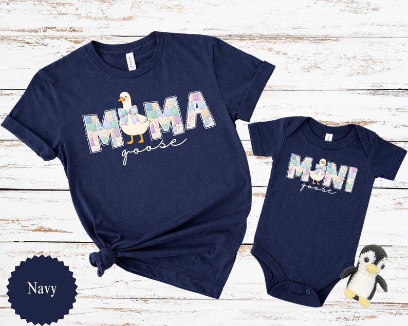 K&ouml;nnte beinhalten: Marineblaues Set aus passenden T-Shirts und Bodys. Das Erwachsenen-Shirt tr&auml;gt die Aufschrift "MAMA goose" mit einer G&auml;nsegrafik. Der Baby-Body tr&auml;gt die Aufschrift "MINI goose" mit einer passenden G&auml;nsegrafik. Ein kleines Pinguin-Spielzeug liegt neben dem Body.