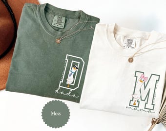 May include: Two Comfort Colors t-shirts, one moss green and one cream, with matching gold necklaces. The green shirt has a white "D" with a goose graphic and the word "dada". The cream shirt has a white "M" with a goose graphic and the word "mama".