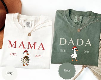 May include: Two Comfort Colors t-shirts, one ivory and one moss green, with the words "MAMA" and "DADA" printed in red and white, respectively. Each shirt features a cartoon goose wearing a Santa hat and festive lights. The year "2025" is also printed on each shirt.