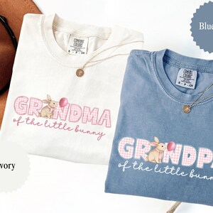 May include: Two Comfort Colors t-shirts, one ivory and one blue jean, featuring the text "Grandma of the little bunny" and "Grandpa of the little bunny" with a bunny graphic. Each shirt has a gold necklace.