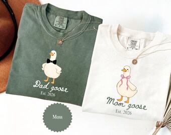 May include: Two Comfort Colors t-shirts, one moss green and one cream, featuring goose illustrations. The green shirt says "Dad goose Est. 2026" and the cream shirt says "Mom goose Est. 2026". Both shirts have a gold necklace.