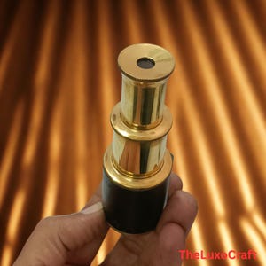 May include: A brass and black telescope with a classic design. The telescope has a cylindrical shape with multiple sections and a small lens at the top. The base is black, and the rest is gold-colored.