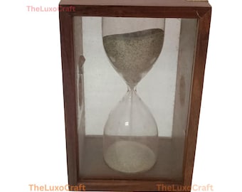 Op de afbeelding: Een houten zandloper in een rechthoekig houten frame met glazen panelen. De zandloper bevat lichtgekleurd zand. Het frame heeft messing hoekaccenten en de tekst "TheLuxoCraft" in de linker- en rechterbenedenhoek.