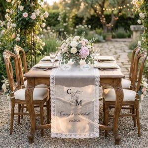 May include: A wooden dining table with four chairs, featuring a white lace table runner printed with the letters C and M, the names Casey & Mitchell, and the text est.2026. A floral centerpiece sits on the table with place settings and name cards.