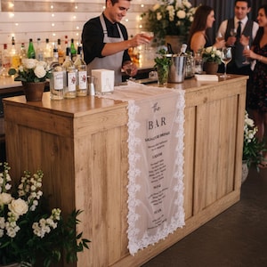 May include: A long, rectangular, sheer white fabric table runner with intricate lace trim along the edges. The runner features black printed text that reads: the BAR, SIGNATURE DRINKS, LIQUOR, WINE, BEER, and a list of various beverage options.