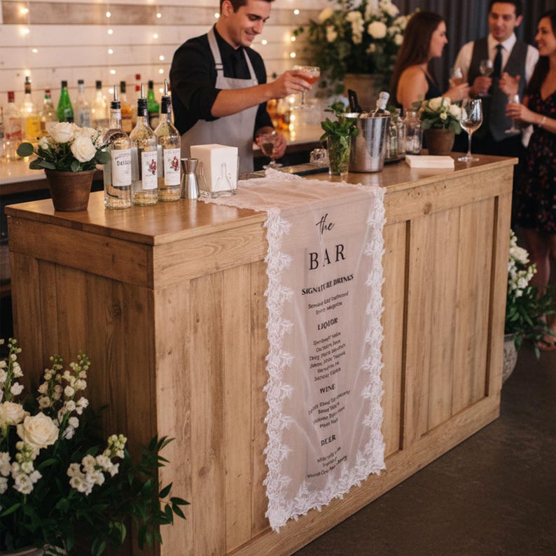 May include: A long, rectangular, sheer white fabric table runner with intricate lace trim along the edges. The runner features black printed text that reads: the BAR, SIGNATURE DRINKS, LIQUOR, WINE, BEER, and a list of various beverage options.