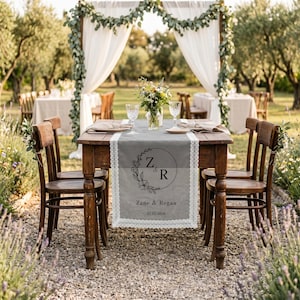 May include: A rectangular gray table runner with white lace trim, featuring a black circular floral wreath design with the initials Z & R, the names Zane & Regan, and the date 12.05.2026 printed in the center on a wooden table.